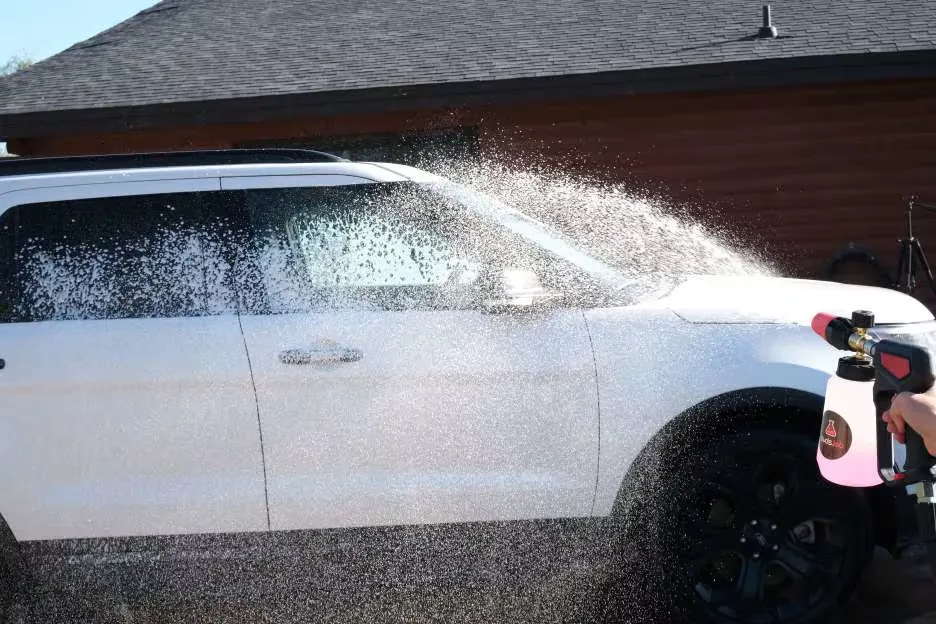 Image of the right side of a white SUV car being sprayed with a foam cleaning solution.